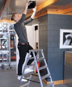 Man staat op een alumexx dubbele trap om een lamp te bevestigen aan het plafond