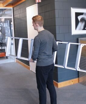 Man met rood haar en grijs vest houd een Alumexx dubbele trap vast om hem te verplaatsen