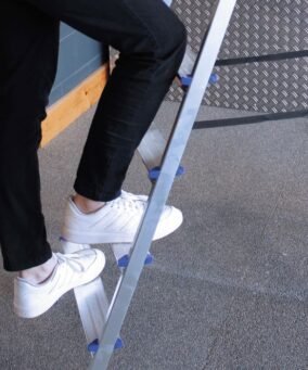 Man met witte sneakers loopt een Alumexx dubbele trap op.